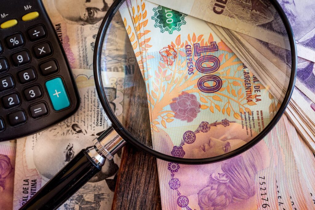 Magnifying glass resting on top of a small stack of Argentinian pesos.