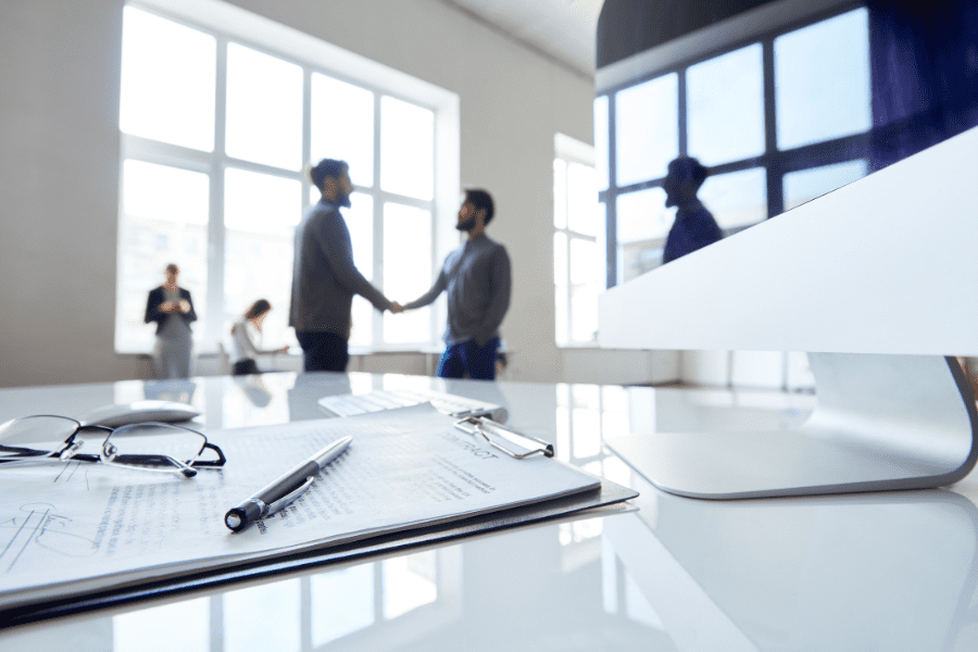 an independent contractor shaking hands with hiring manager in the background of a singed contract and pen on table