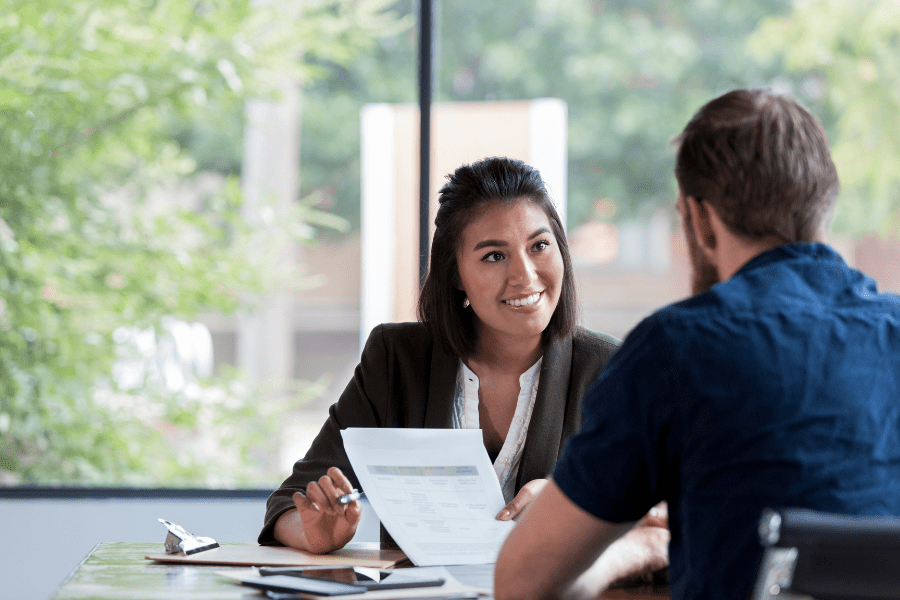 Female Latin American human resource manager discussing LATAM hiring and firing policies with male employee while showing a document